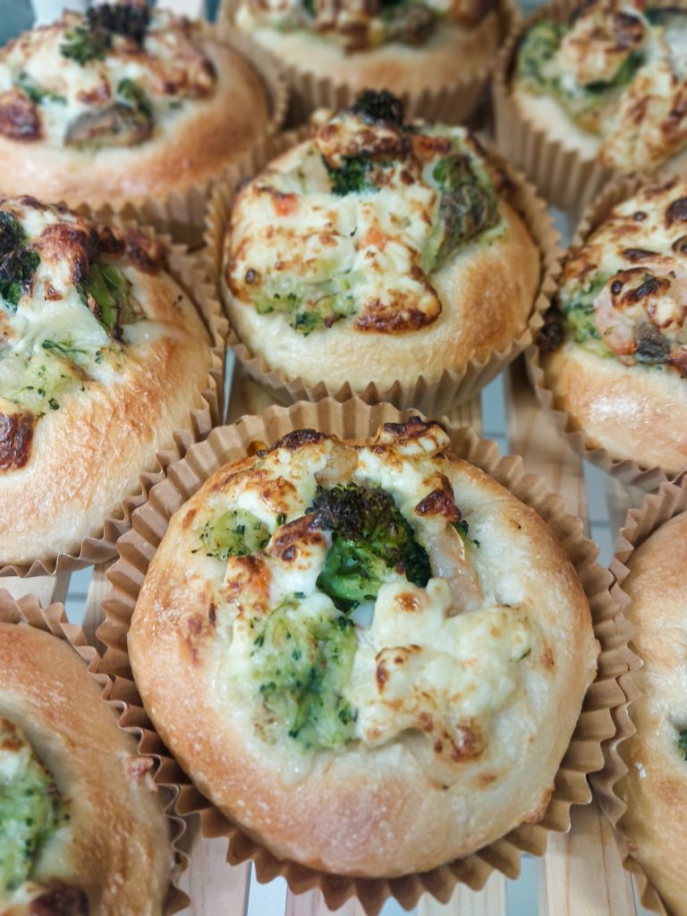 こまいぬベーグル堂の焼き立てブロッコリーチーズパン。ブロッコリーとチーズがたっぷりのった惣菜パンがクラフト紙カップに並ぶ様子