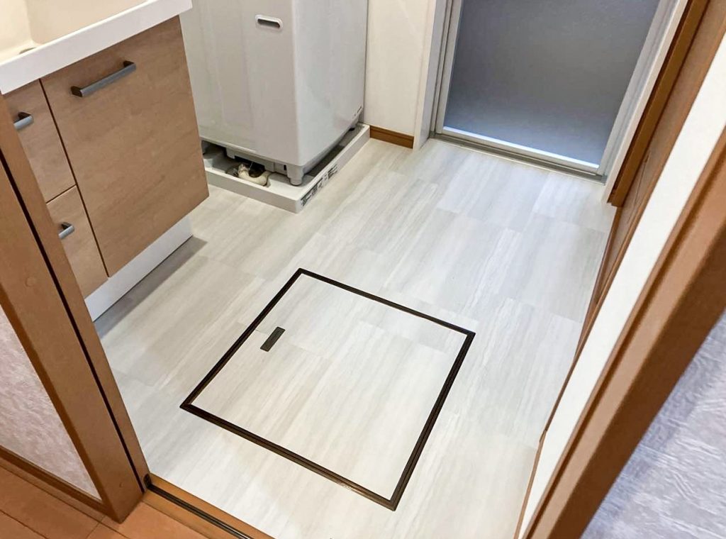 柏市M様邸の洗面室リフォーム後の床。クッションフロアからフロアタイルに張り替え済み。明るい木目調で清潔感があり点検口も設置