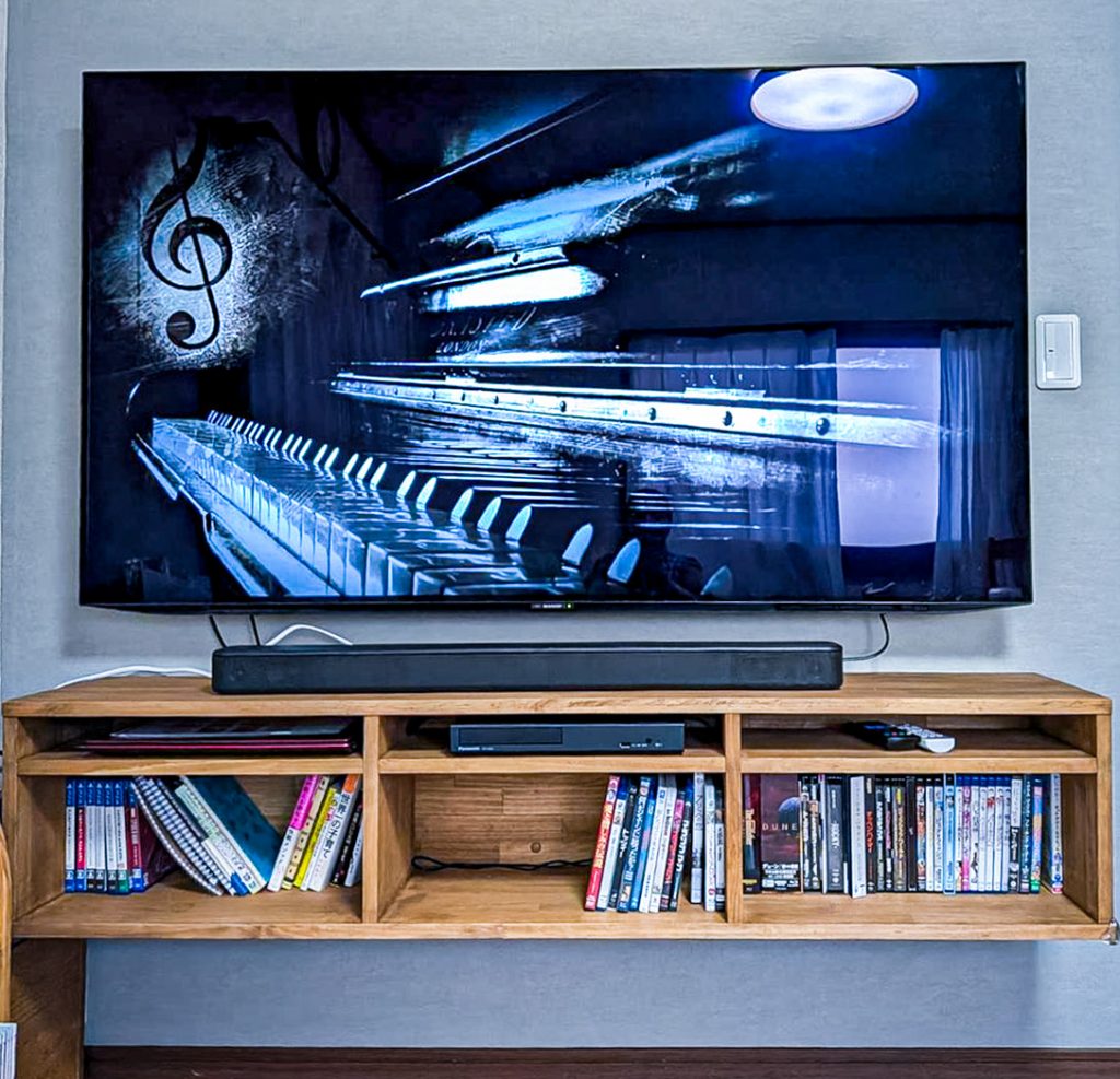 鎌ケ谷市M様邸の壁掛けテレビと造作テレビボード完成写真。正面から見た全体像。無垢材チーク色のテレビボードに本やCDが収納されすっきりとしたリビング