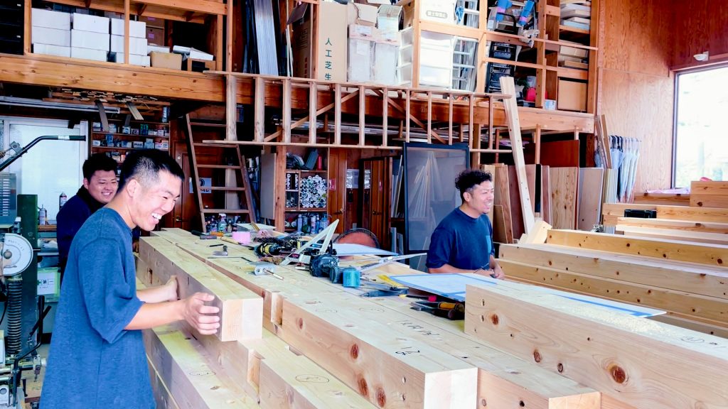 小川工務店の作業場で若手大工が笑顔で木材を加工している