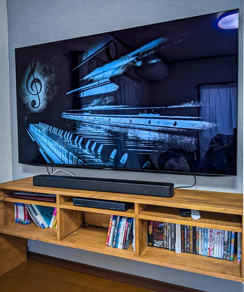 鎌ケ谷市M様邸の造作テレビボードを斜めから見た完成写真。無垢材のチーク色テレビボードと壁掛けテレビの組み合わせが美しいリビング空間