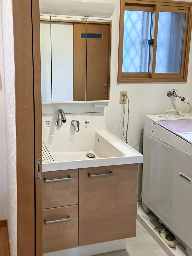 柏市M様邸に設置したリクシル洗面化粧台ピアラ。三面鏡裏収納付きで木目調の扉がナチュラルな印象。窓には断熱用の内窓も設置済み