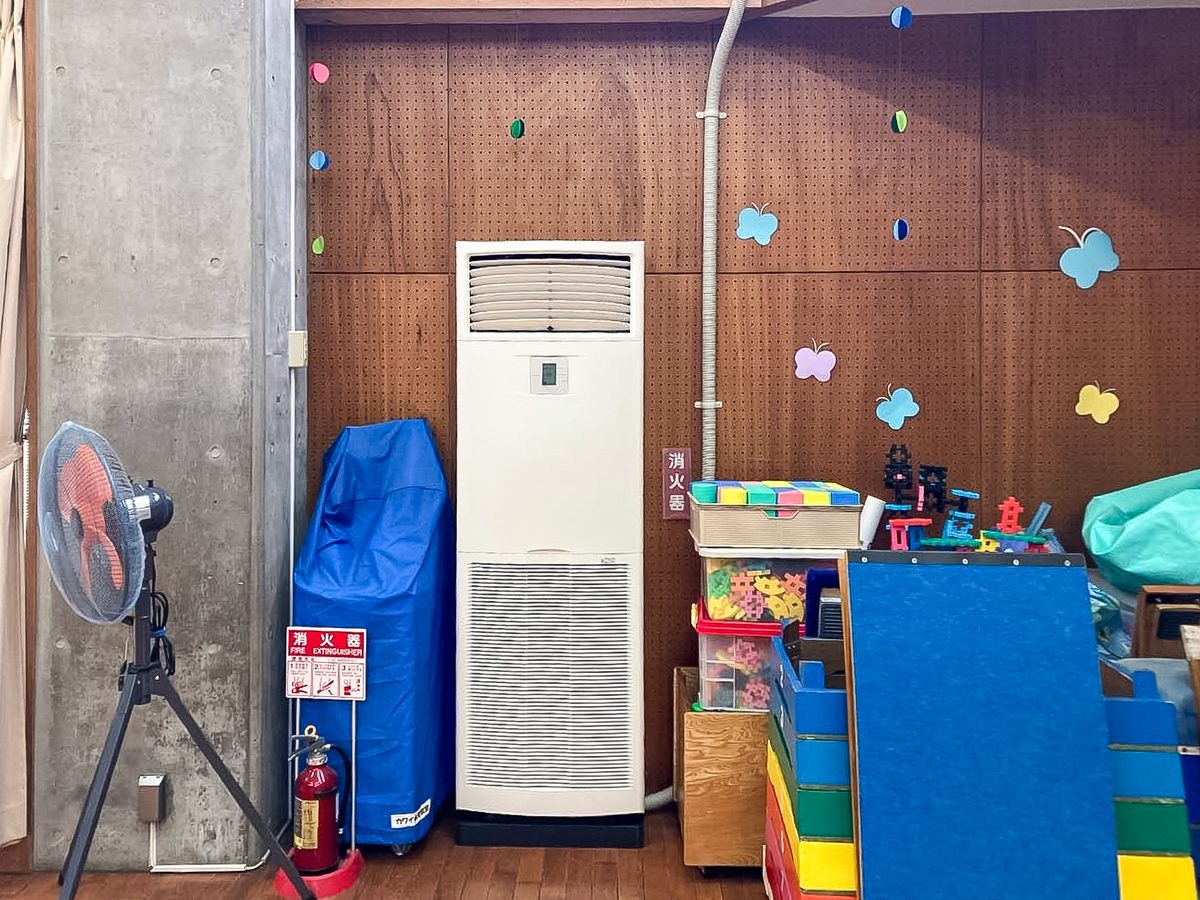 柏市晴山幼稚園の体育館に設置した床置形エアコンの室内機。柱の脇に据え付け、遊具や扇風機と並ぶ