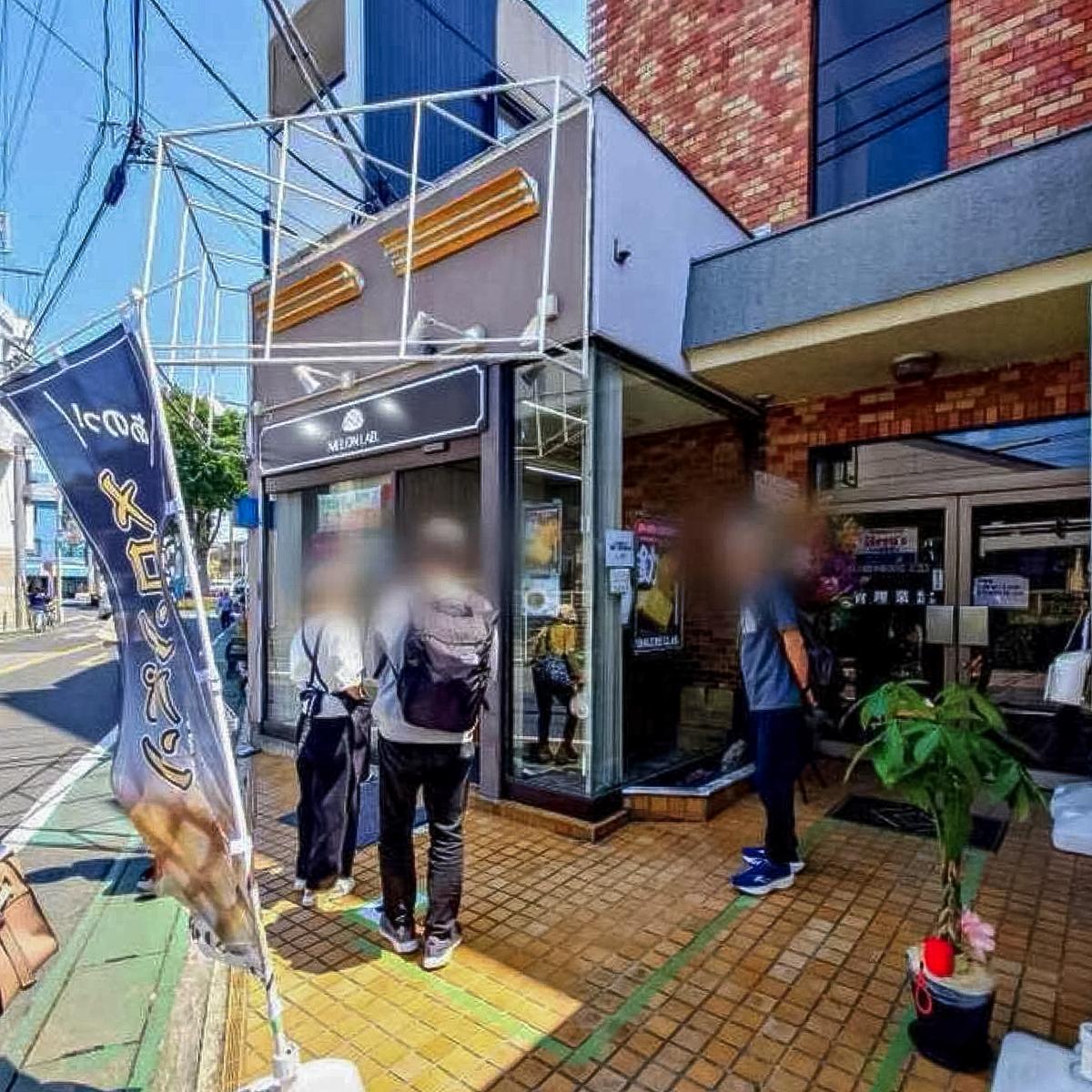 松戸市メロンLAB上本郷駅前店の開店後の外観。のぼりが立ち、窓際のショーケースにお客さんが並ぶ